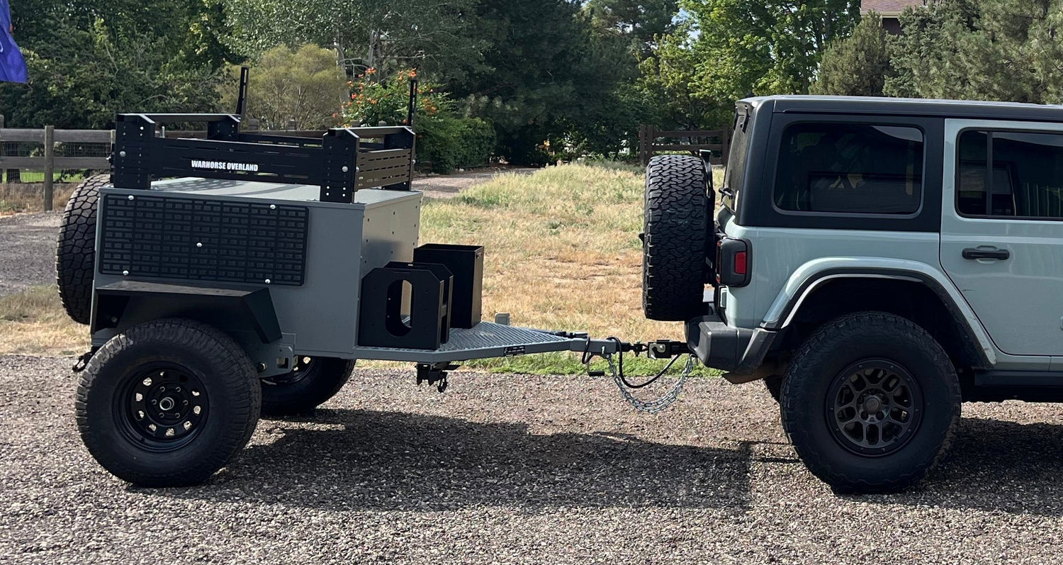Jeep towing a camper trailer on a gravel road with trees in the background