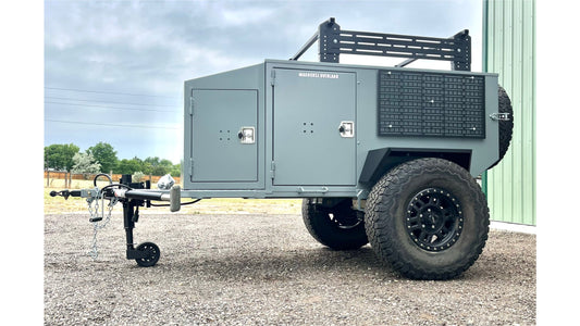 Gray off-road trailer with a generator and equipment on a gravel surface.