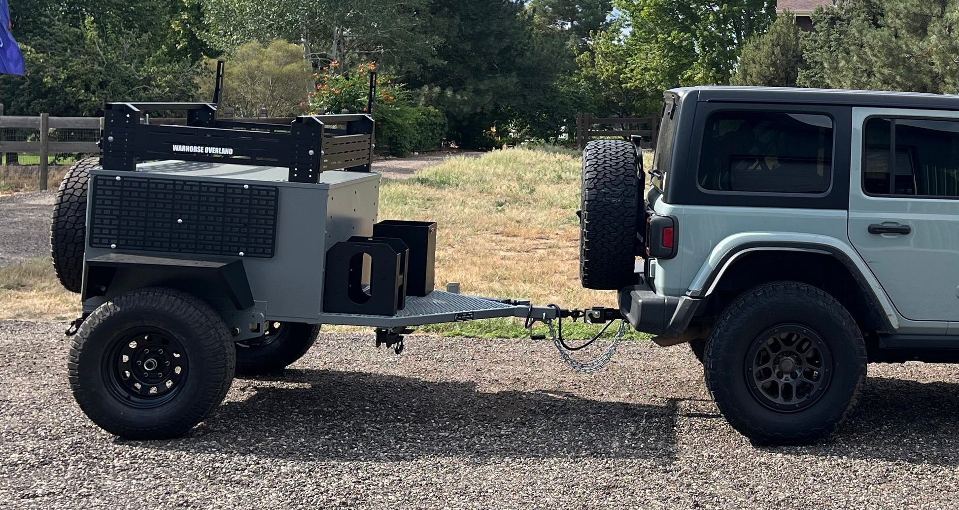 Jeep towing a camper trailer on a gravel road with trees in the background